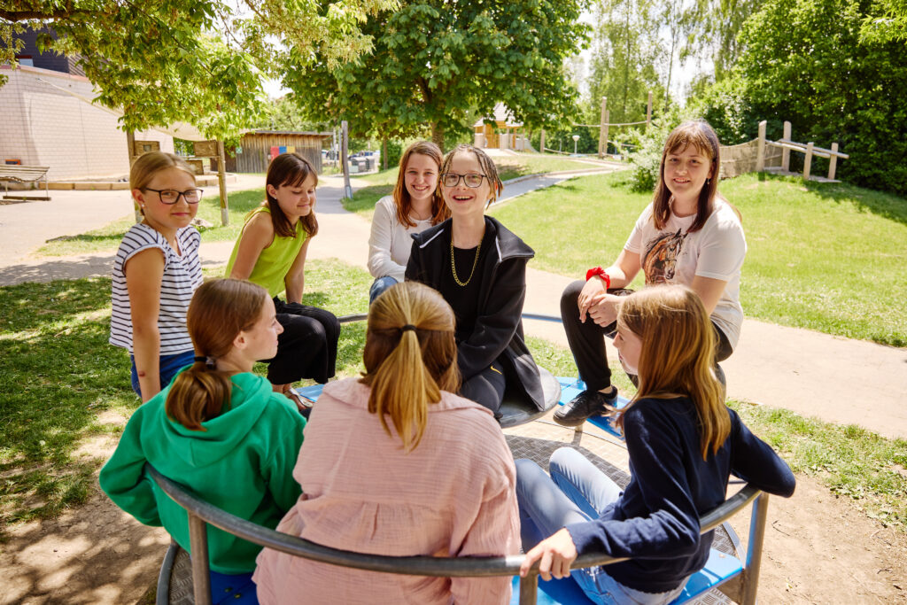Jugendliche sitzen gemeinsam auf einem Karussell auf dem Schulhof des Oberlin-Schulverbunds.