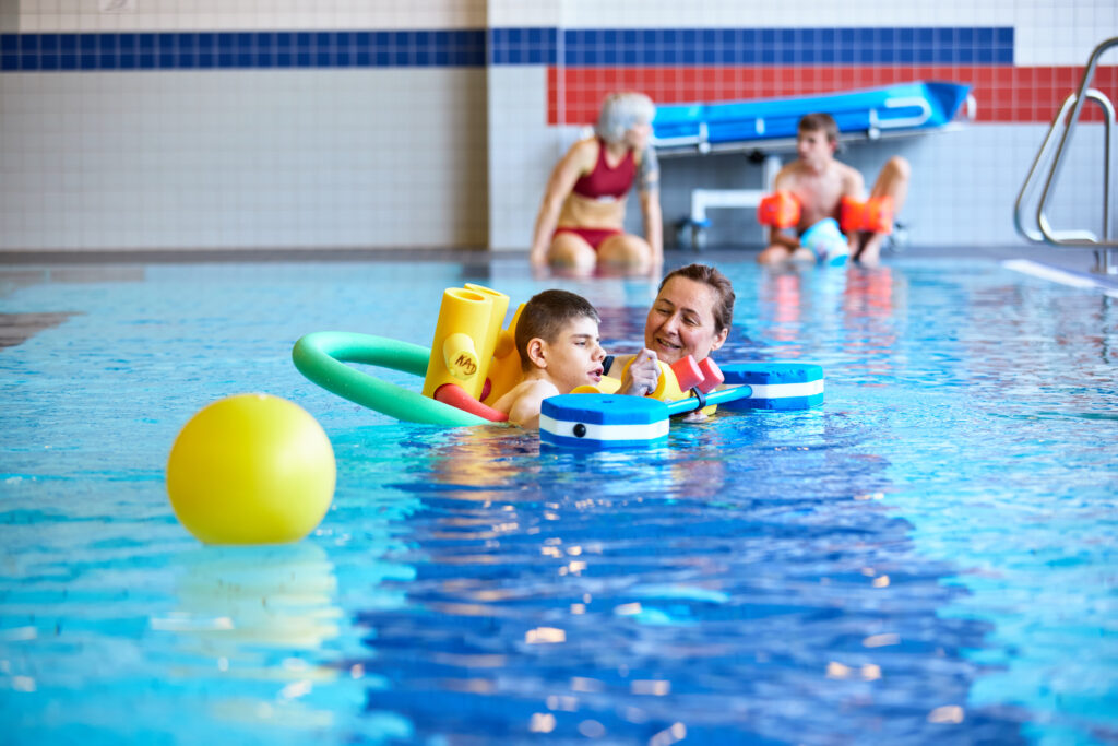 Zwei junge Menschen und zwei Lehrkräfte beim heiltherapeutischen Schwimmen im Wassertropfen-Bad.